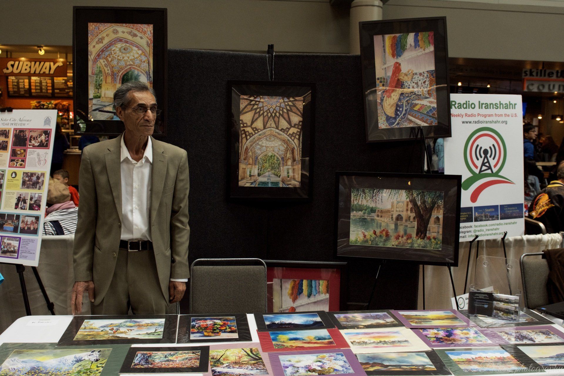 A man in a suit stands in front of a table with paintings on it