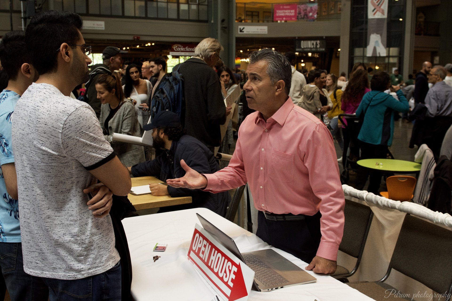 A man in a pink shirt is talking to a group of people at a table.