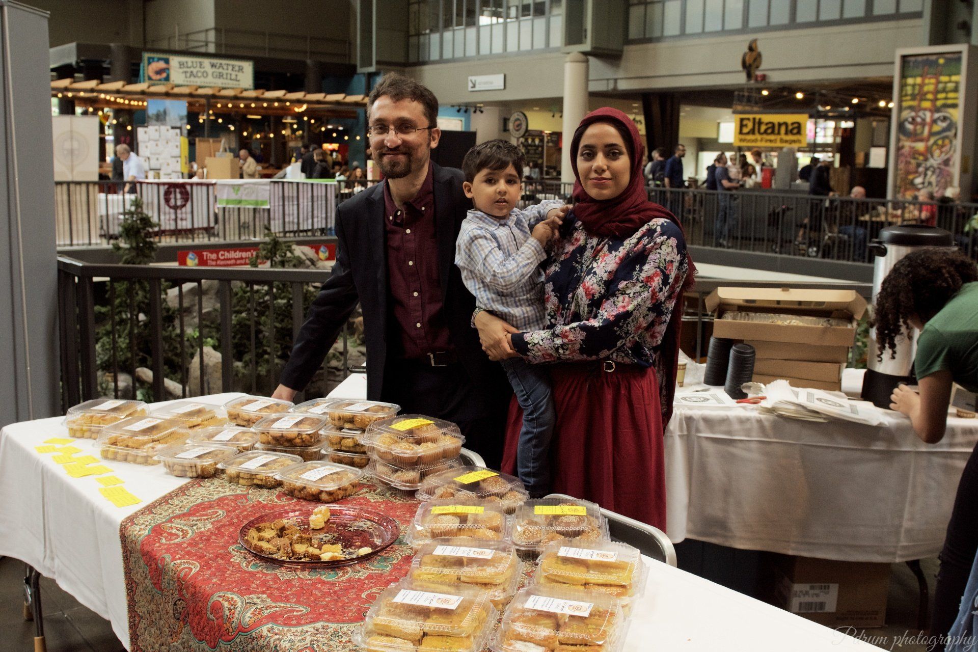 A man and woman are holding a child in front of a table of food.