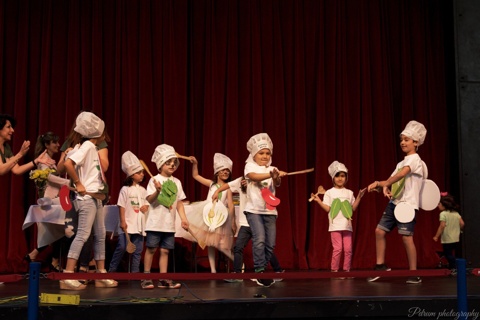 A group of children wearing chef hats and aprons are dancing on a stage.