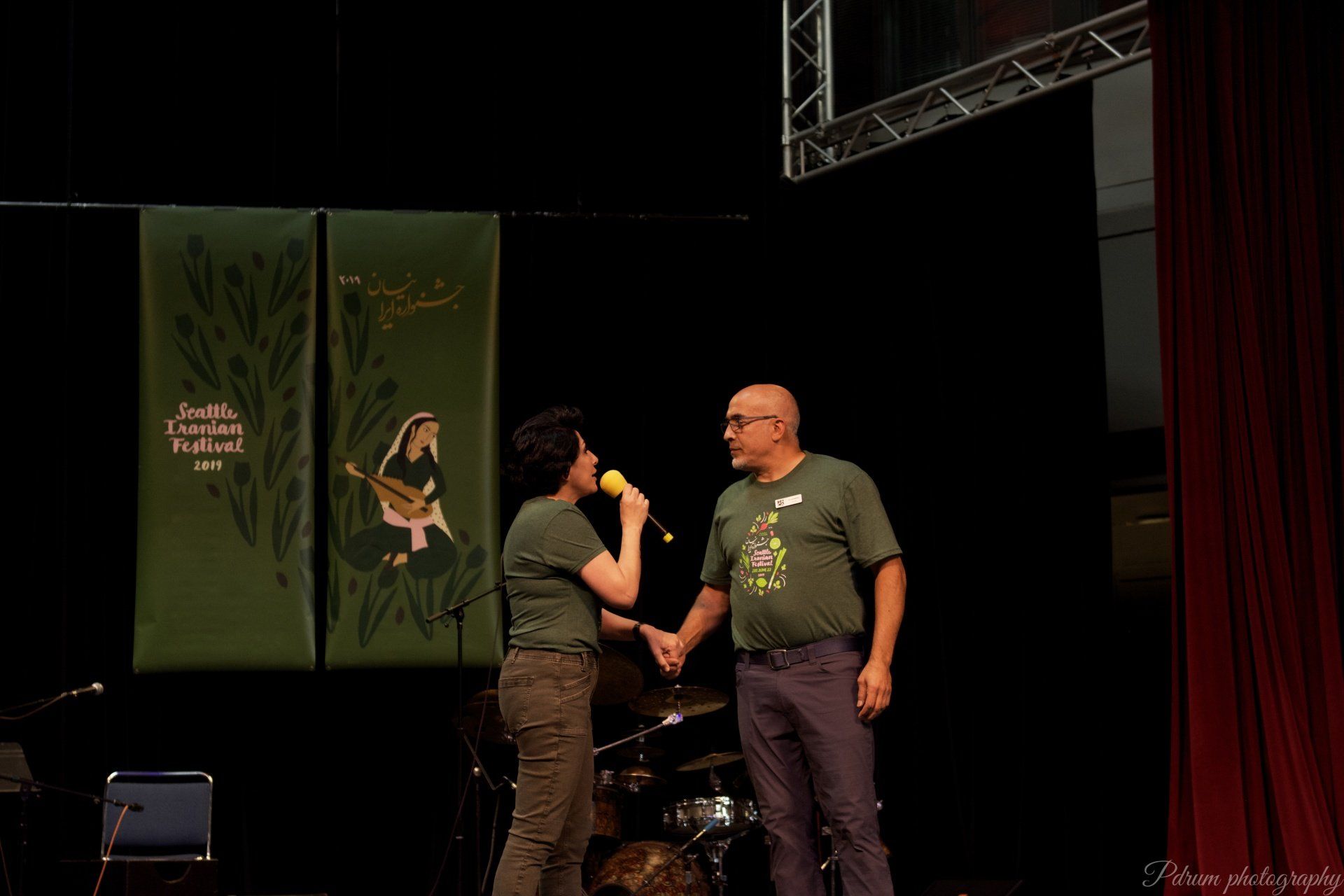 A woman is holding a microphone and shaking hands with a man on a stage.