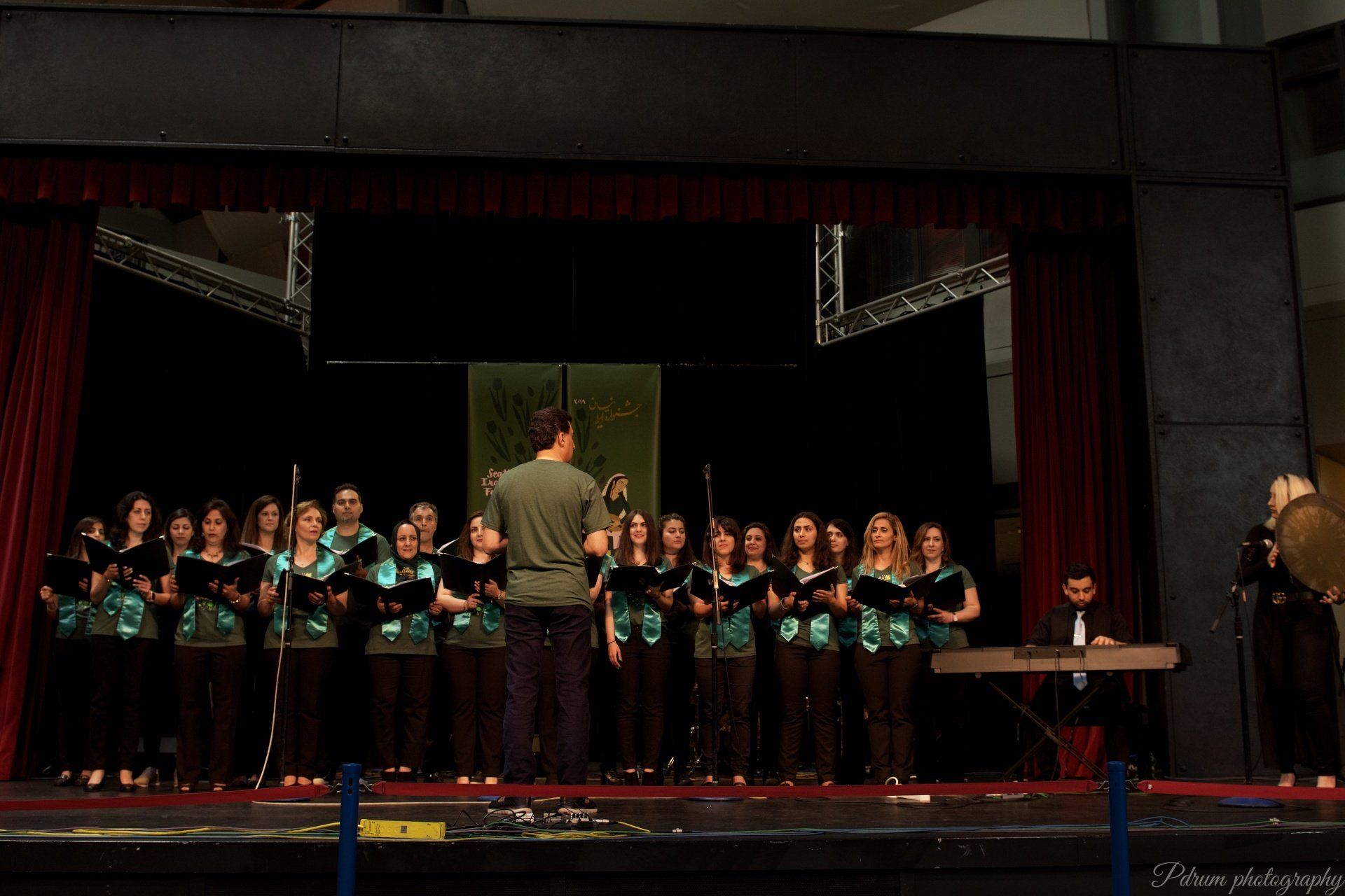 A group of people singing on a stage with a man standing behind them