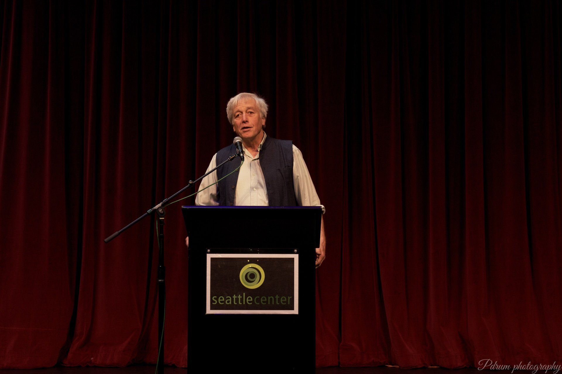 A man is standing at a podium speaking into a microphone.