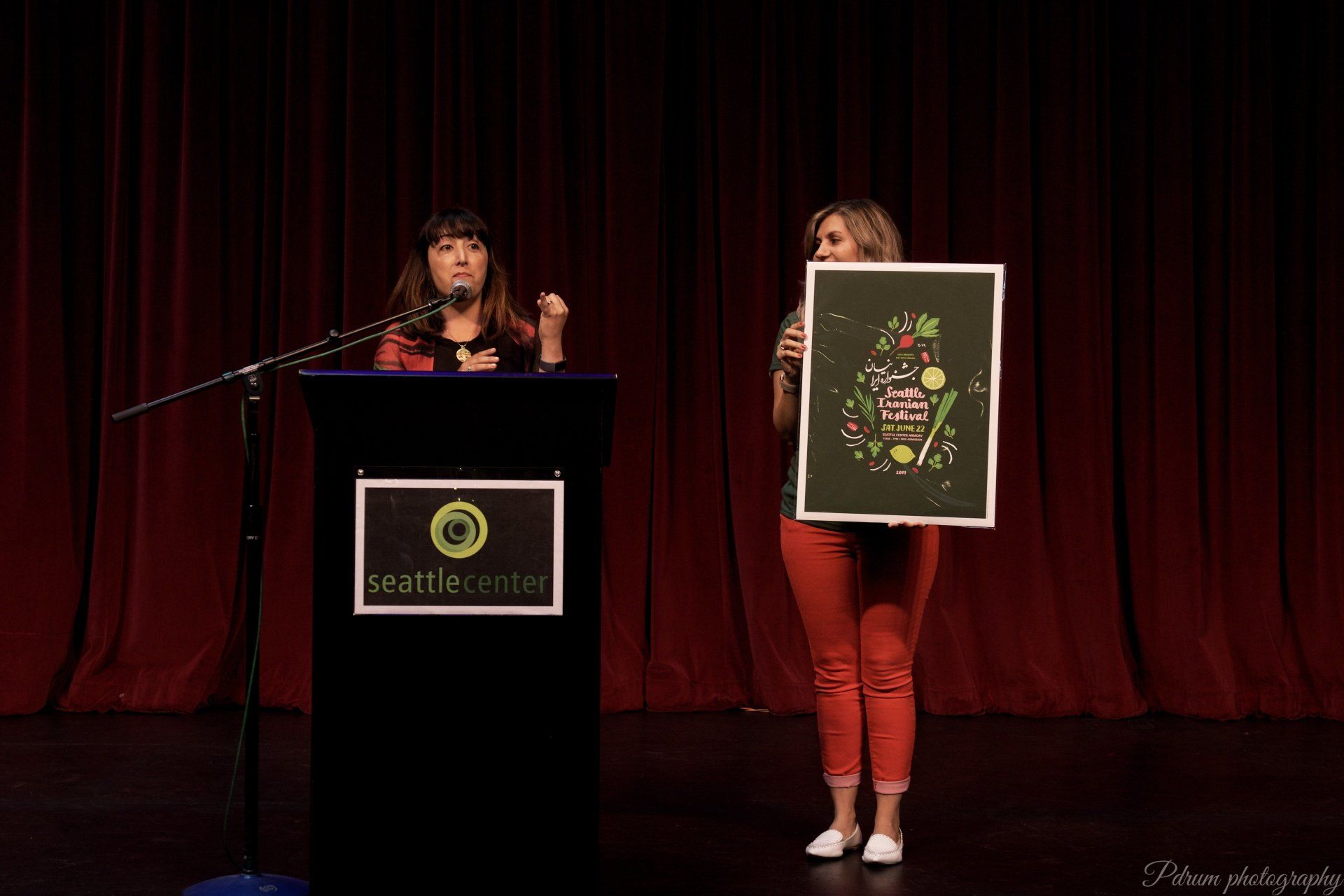 Two women are standing at a podium on a stage holding a picture.