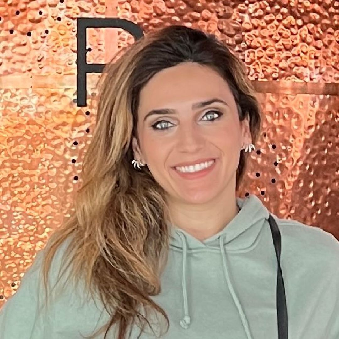 a woman in a green hoodie is smiling in front of a copper wall .