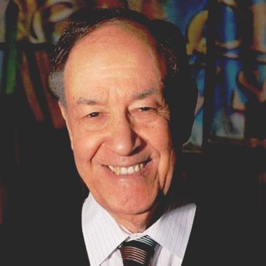 A man in a suit and tie smiles in front of a painting