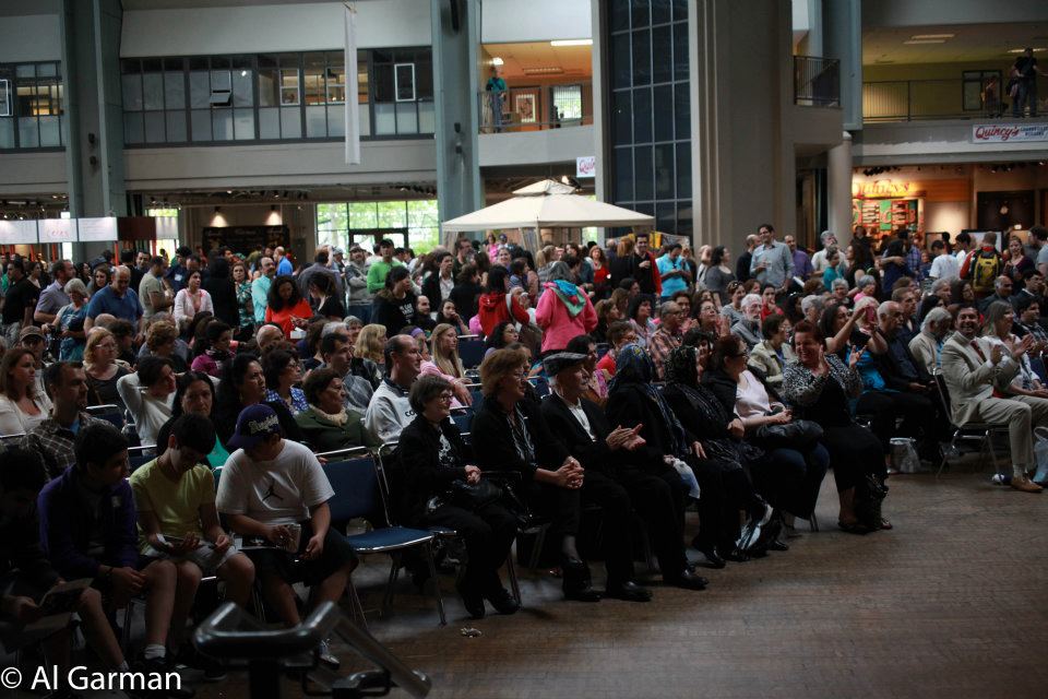 A large group of people are sitting in a large room with a sign that says al carrion