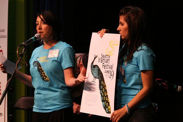 Two women in blue shirts are holding a peacock poster