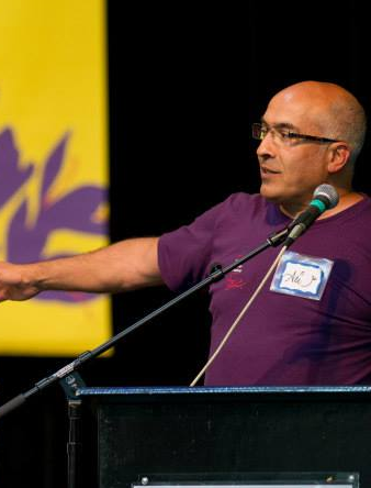 A man in a purple shirt is speaking into a microphone