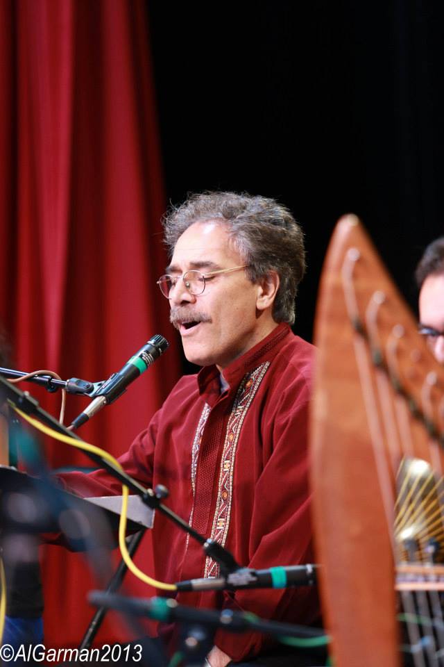 A man singing into a microphone while playing a harp