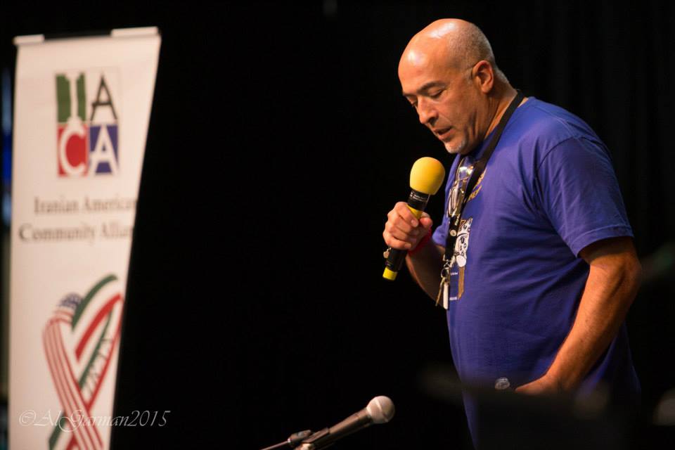 A man in a blue shirt is speaking into a microphone.