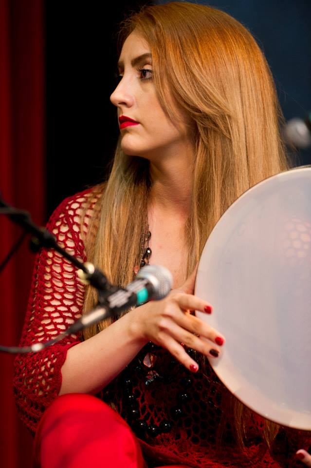 A woman is playing a drum in front of a microphone.