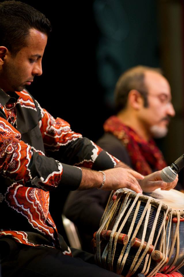 A man is playing a drum with a microphone in his hand.