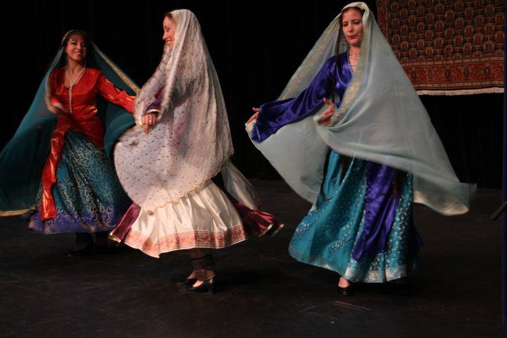 Three women in traditional dresses are dancing on a stage