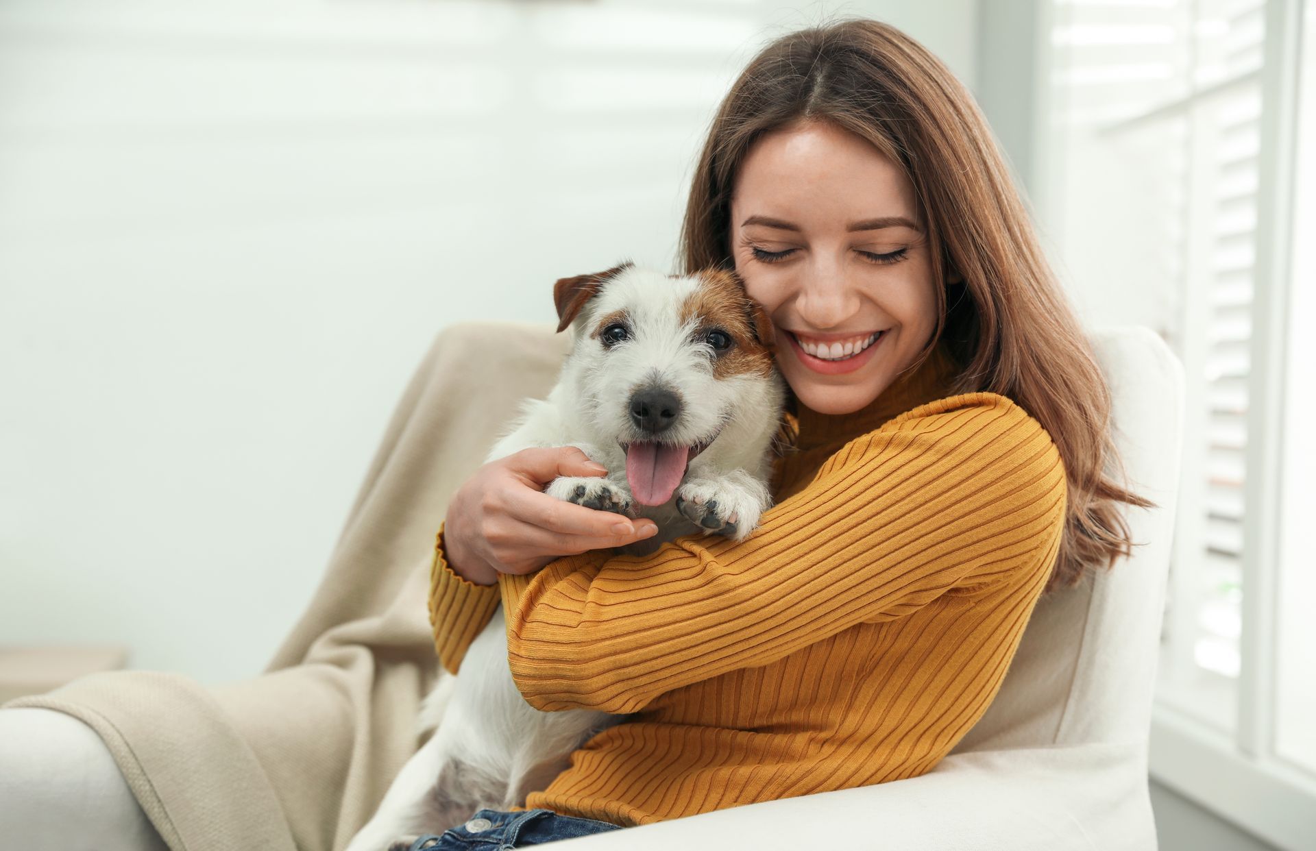 Woman hugging a small, white and brown dog while smiling in a well-lit living room.