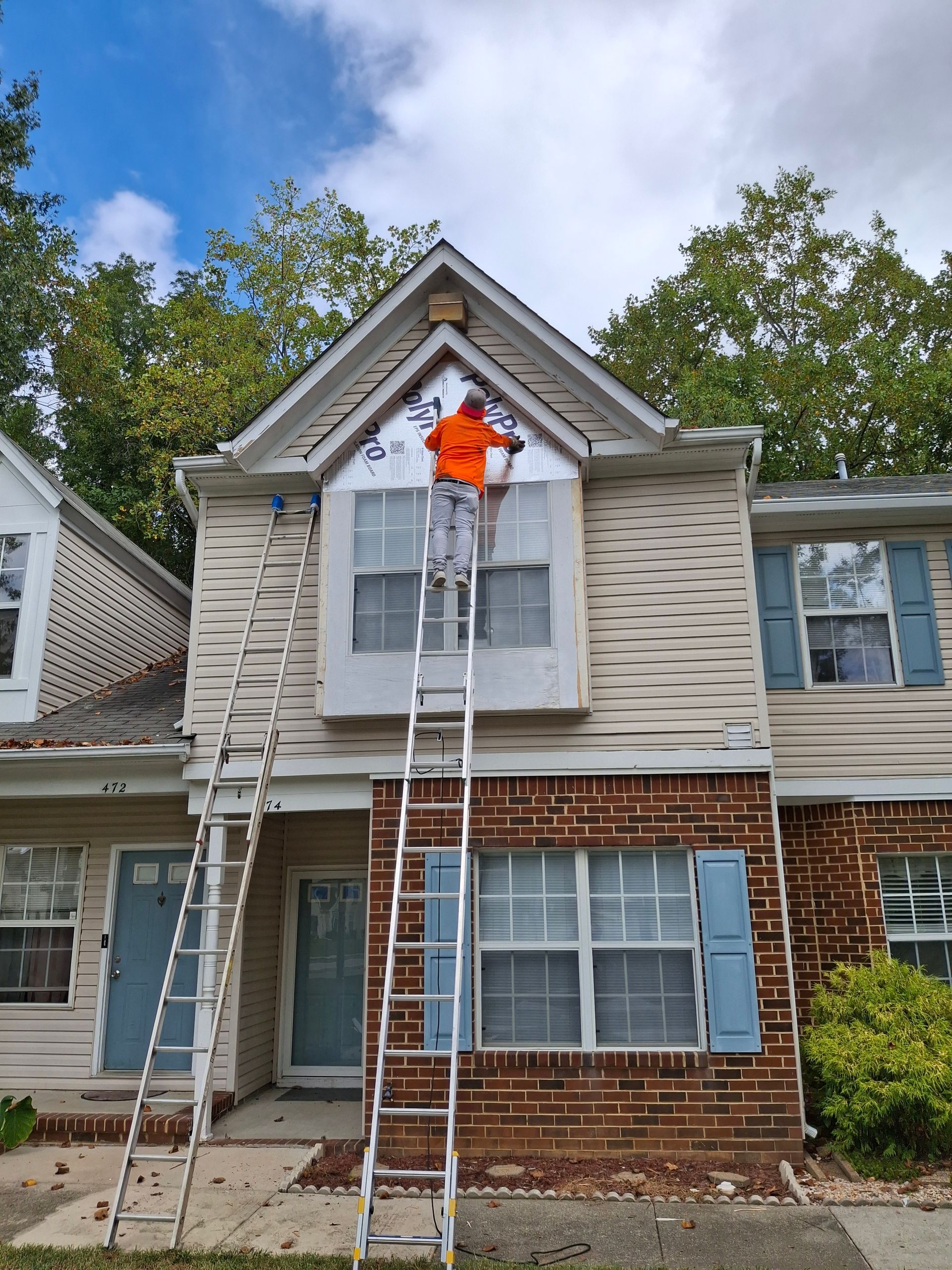 A man is standing on a ladder painting a house.