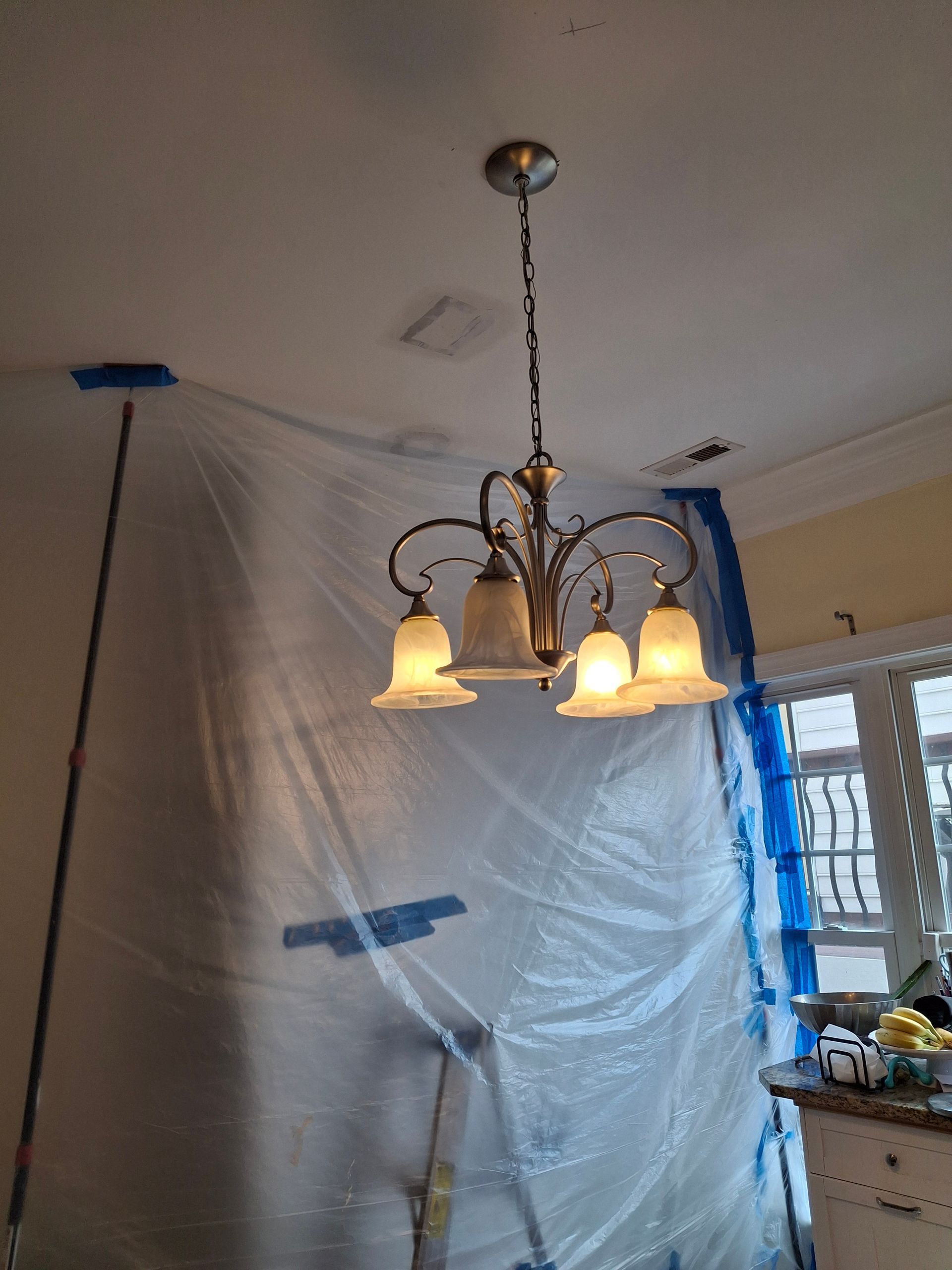 A chandelier is hanging from the ceiling in a room covered in plastic.