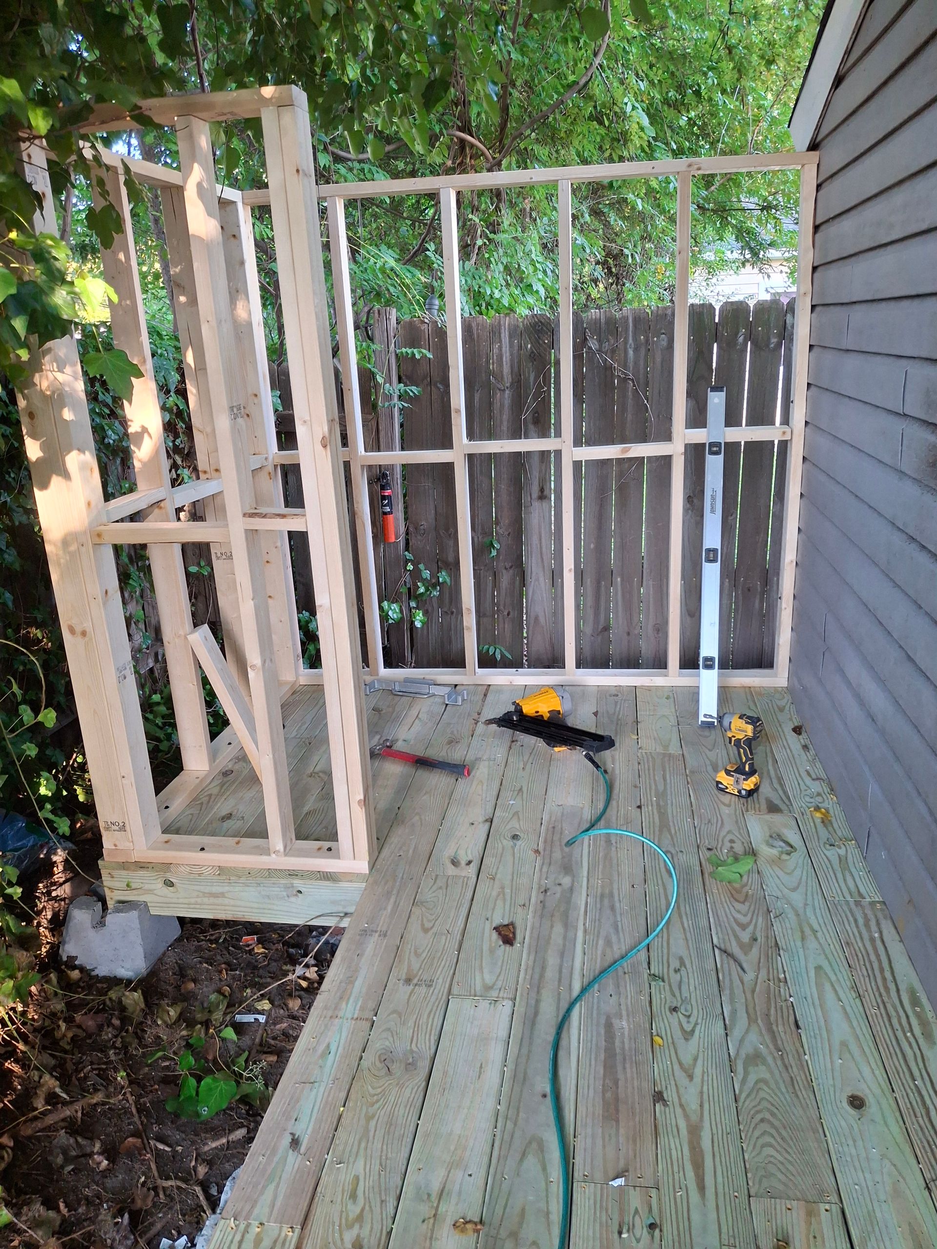 A wooden structure is being built on a wooden deck in front of a fence.