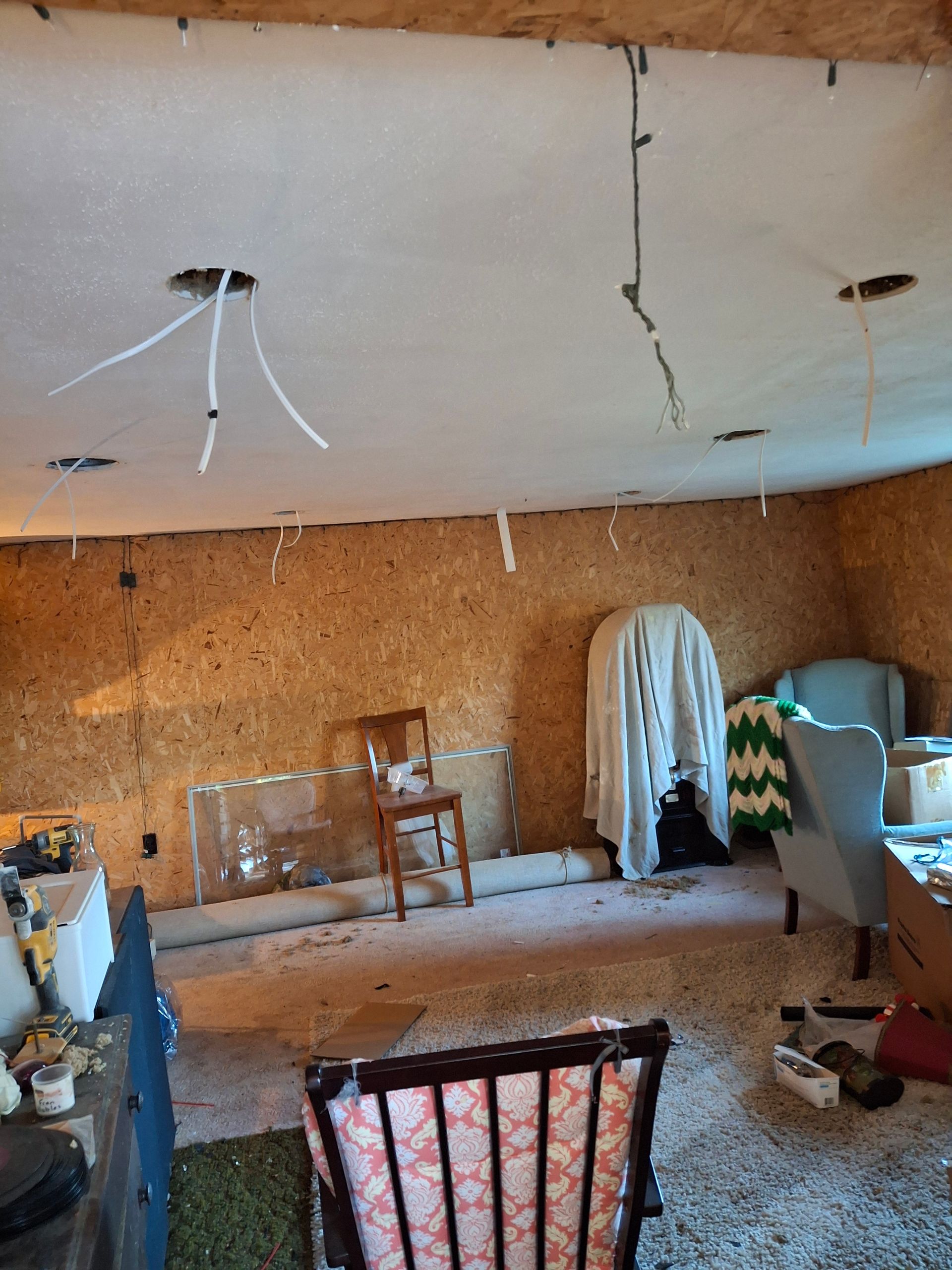 A living room with chairs , a table , and a ceiling with wires hanging from it.