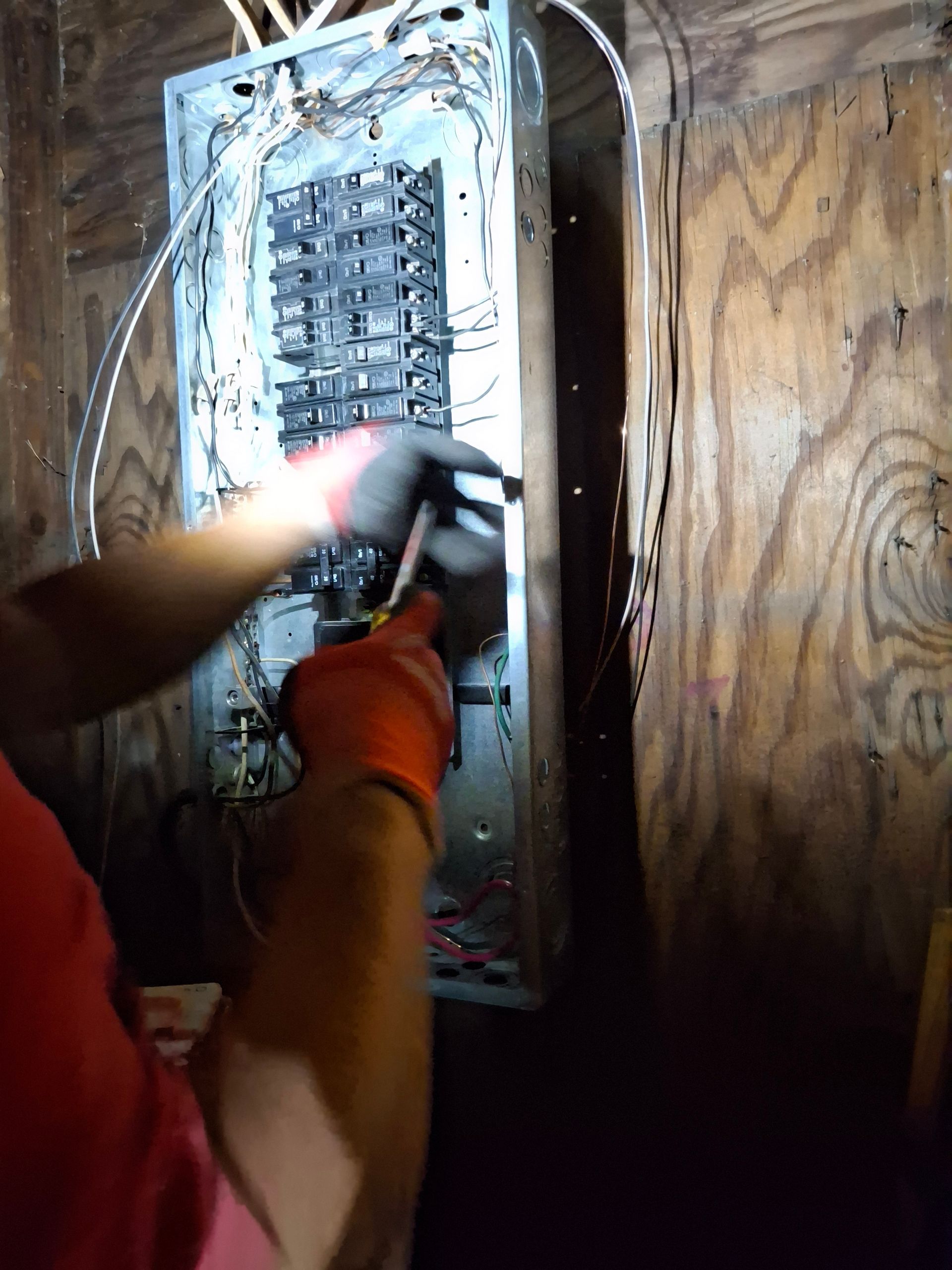 A person is working on an electrical box with a flashlight.