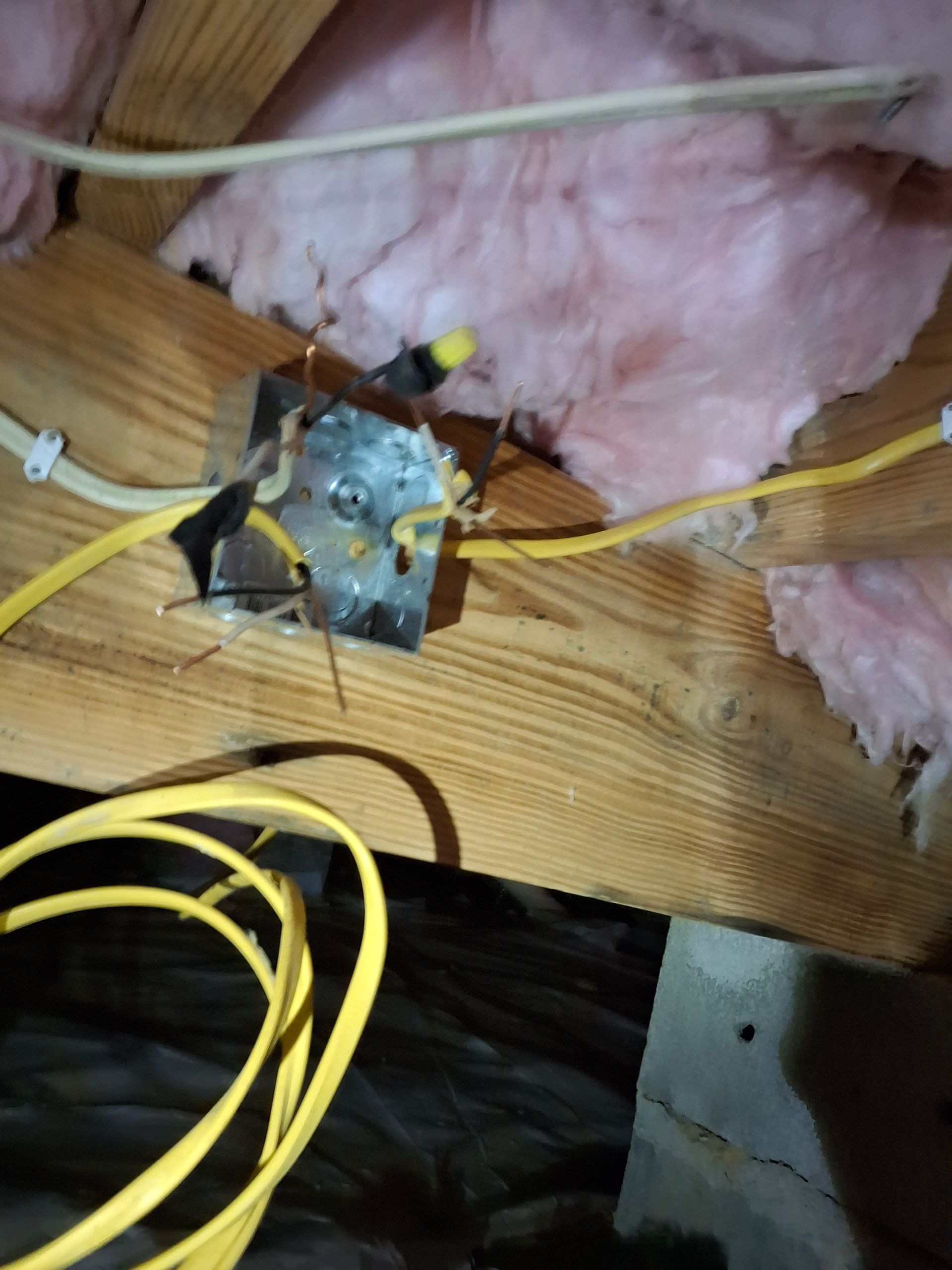 A box with wires coming out of it is in an attic