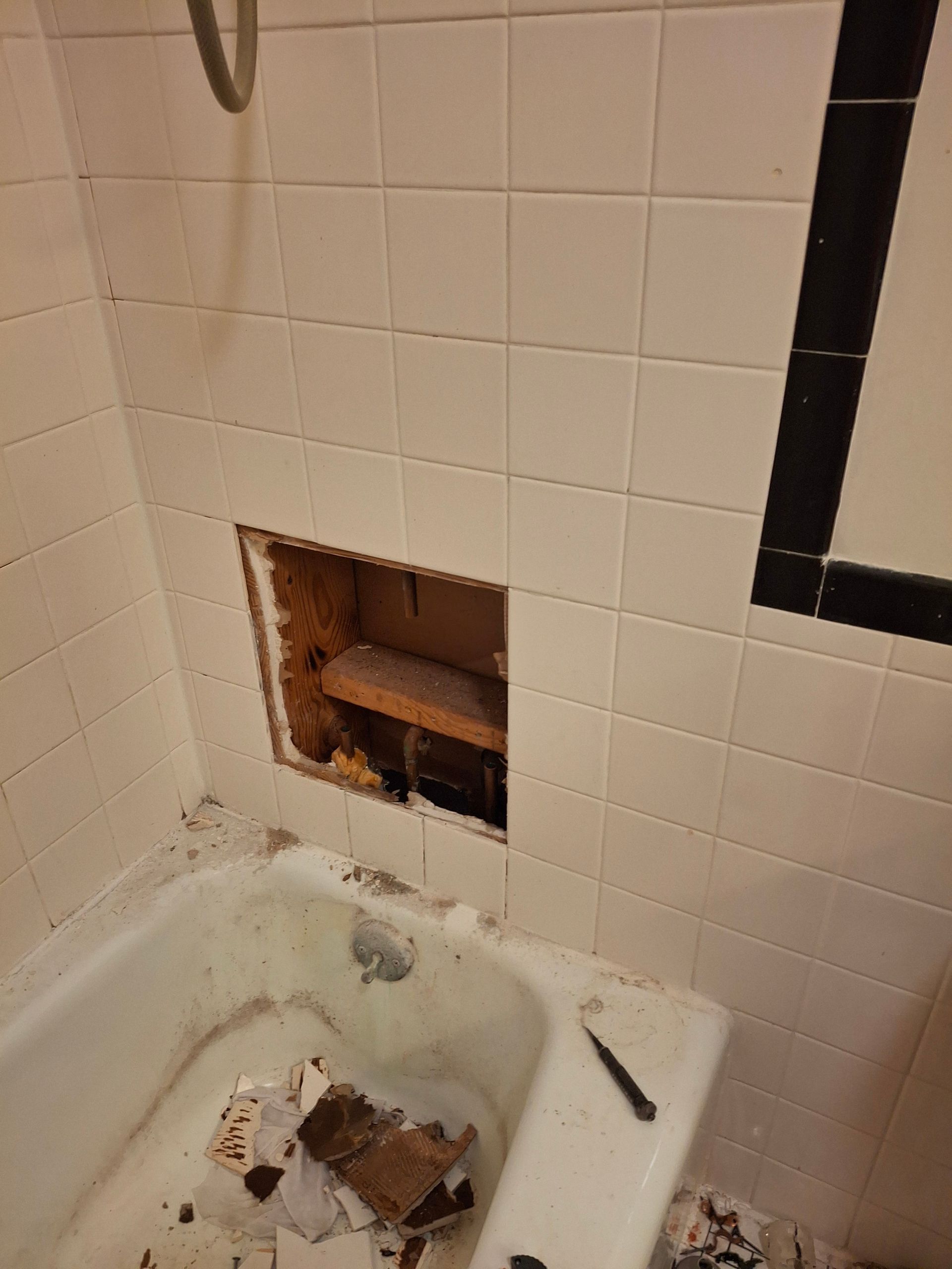 A bathtub in a bathroom with a hole in the wall.