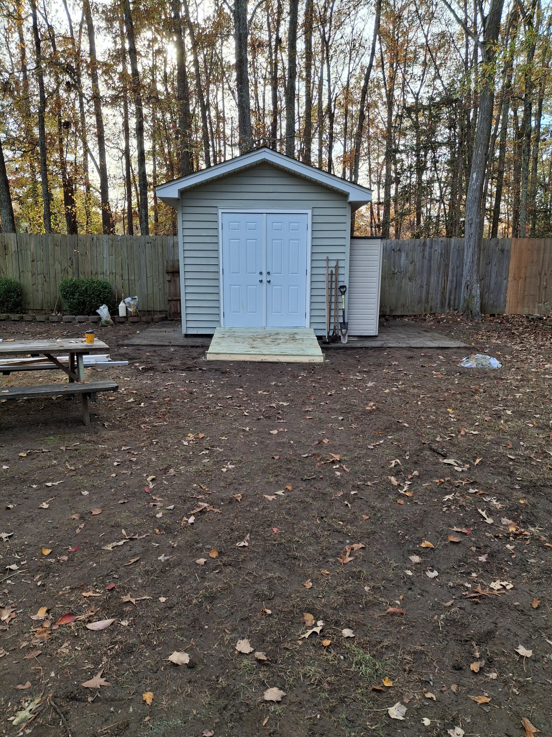A small shed is sitting in the middle of a yard next to a picnic table.