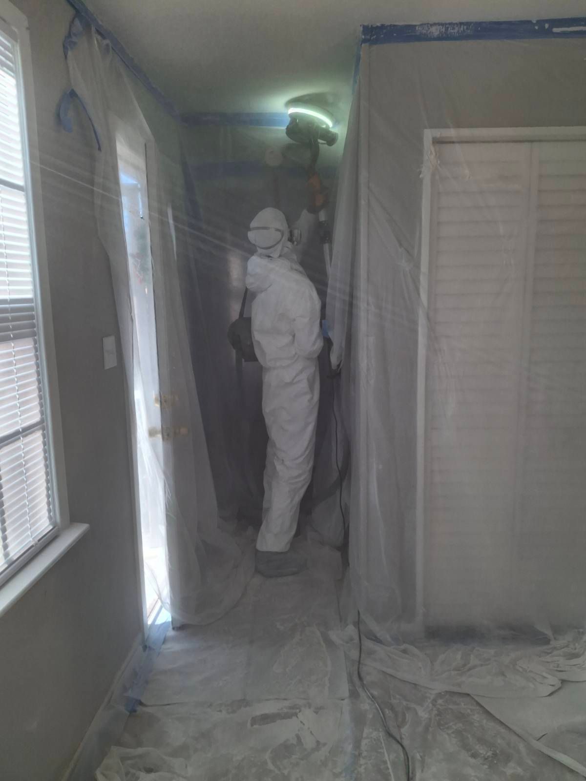A man in a protective suit is standing in a room covered in plastic.