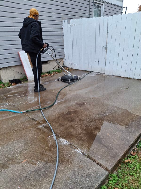 A man is cleaning a concrete driveway with a pressure washer.