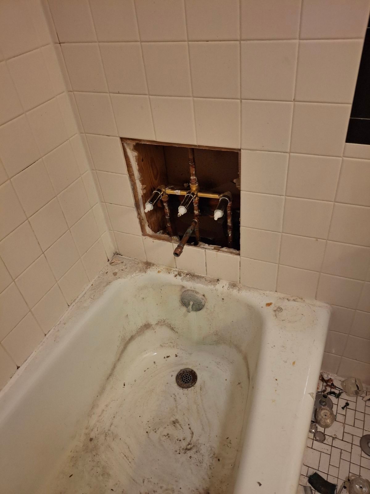 A bathtub in a bathroom with a hole in the wall.