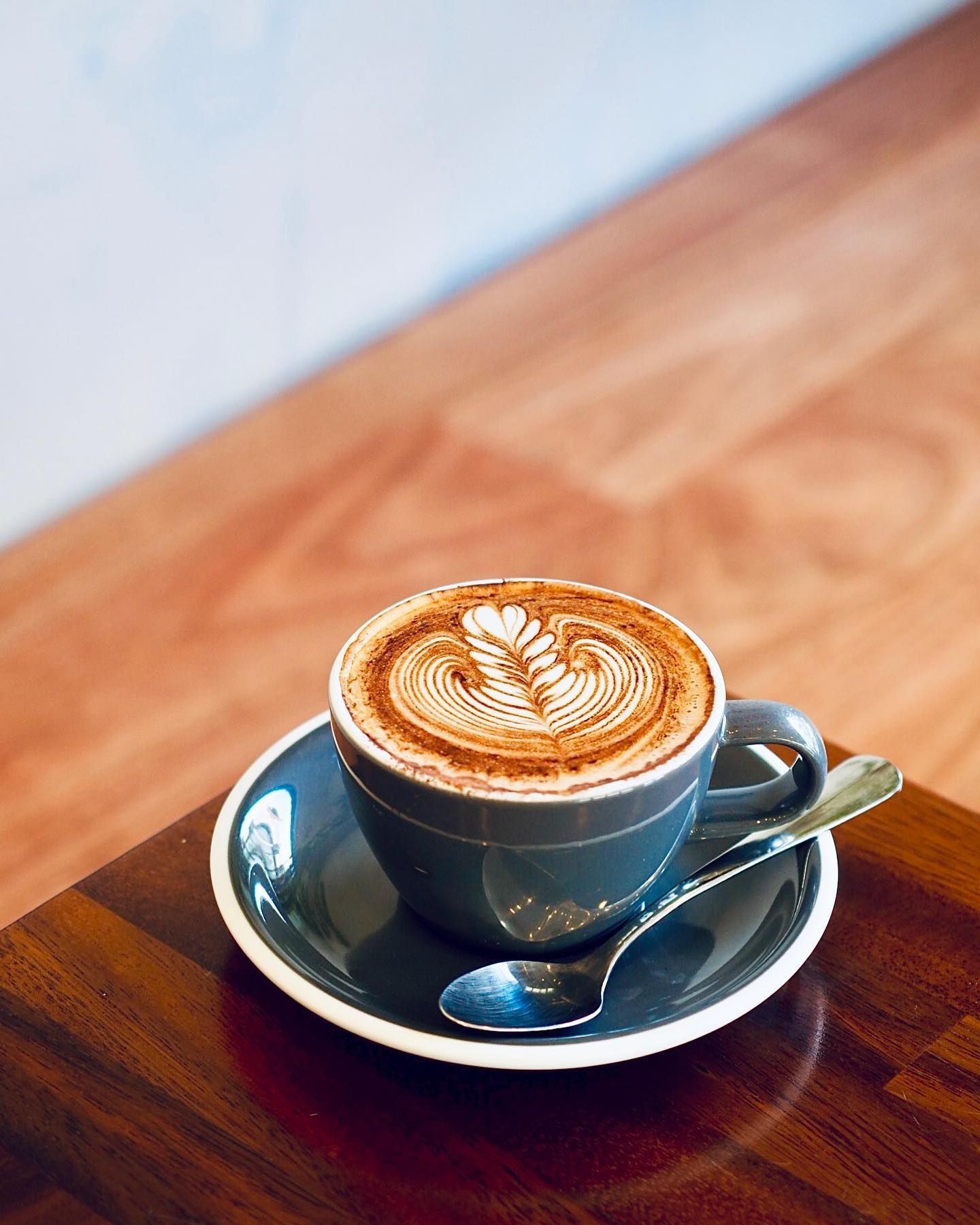 A cup of cappuccino on a saucer with a spoon on a wooden table.