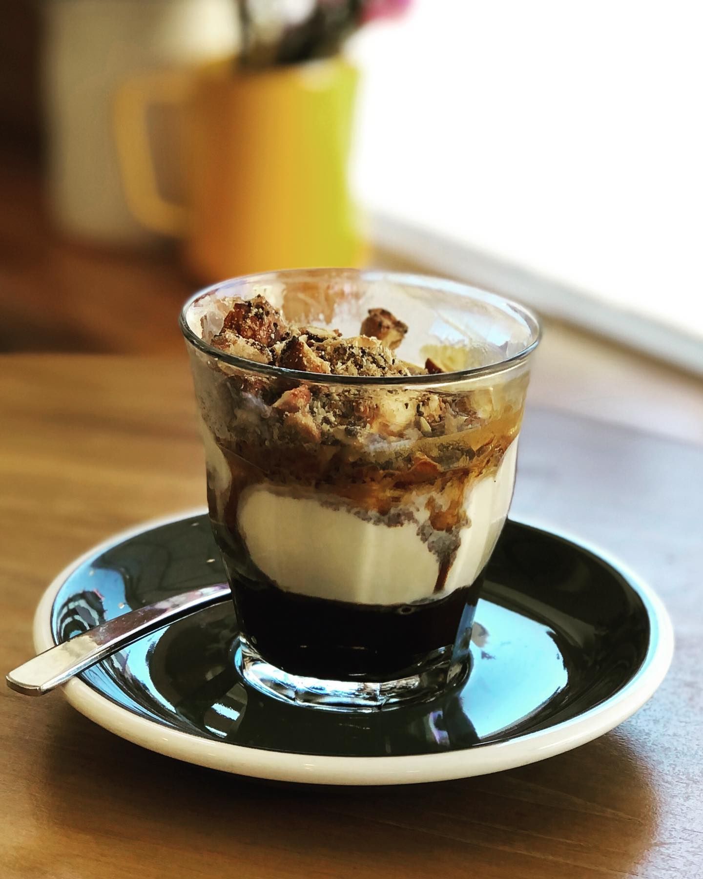 A cup of dessert with a spoon on a saucer on a table.