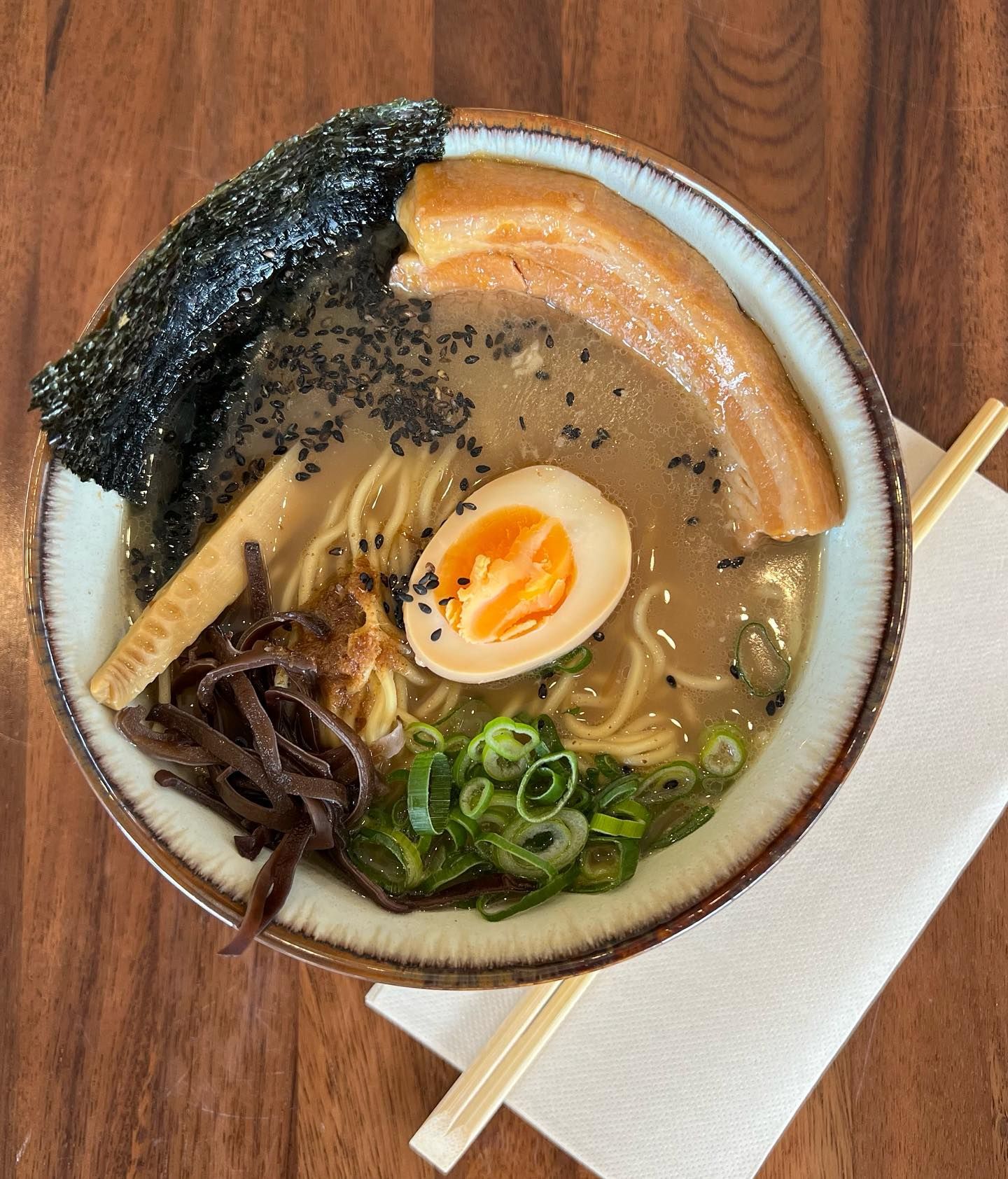 A bowl of ramen with noodles , eggs , meat and seaweed on a wooden table.