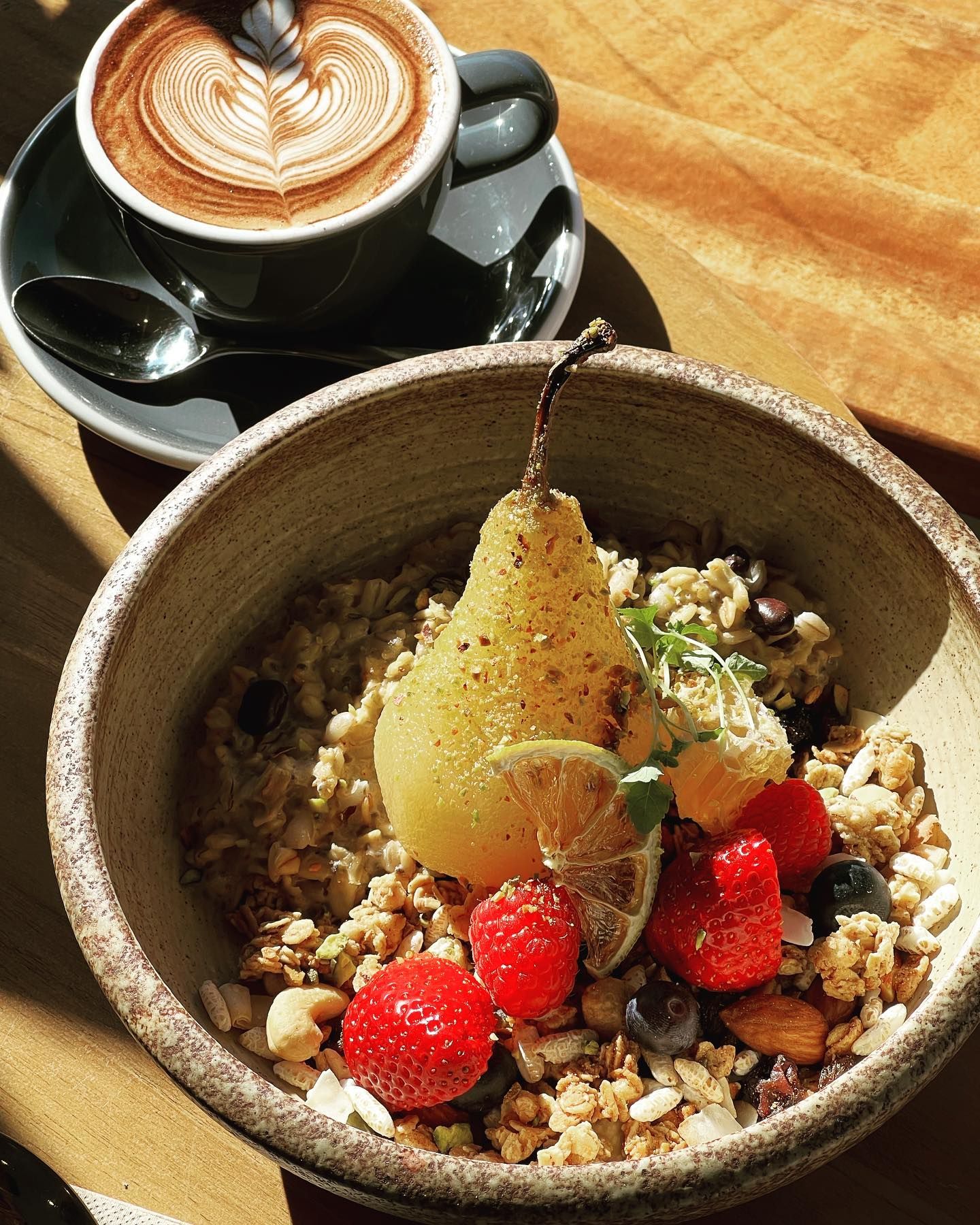 A bowl of granola with fruit and a cup of coffee on a table.