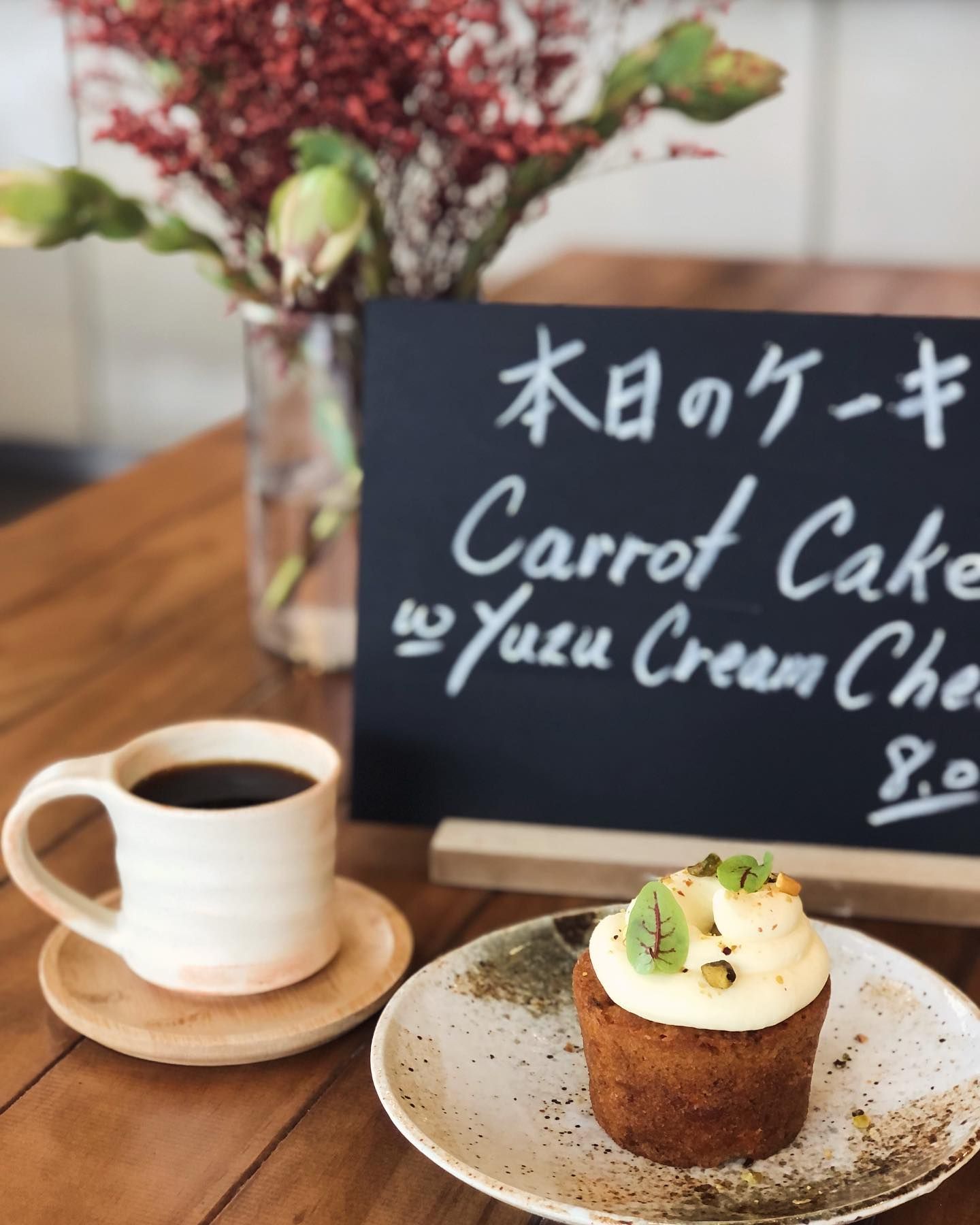 A sign that says carrot cake on it next to a cup of coffee