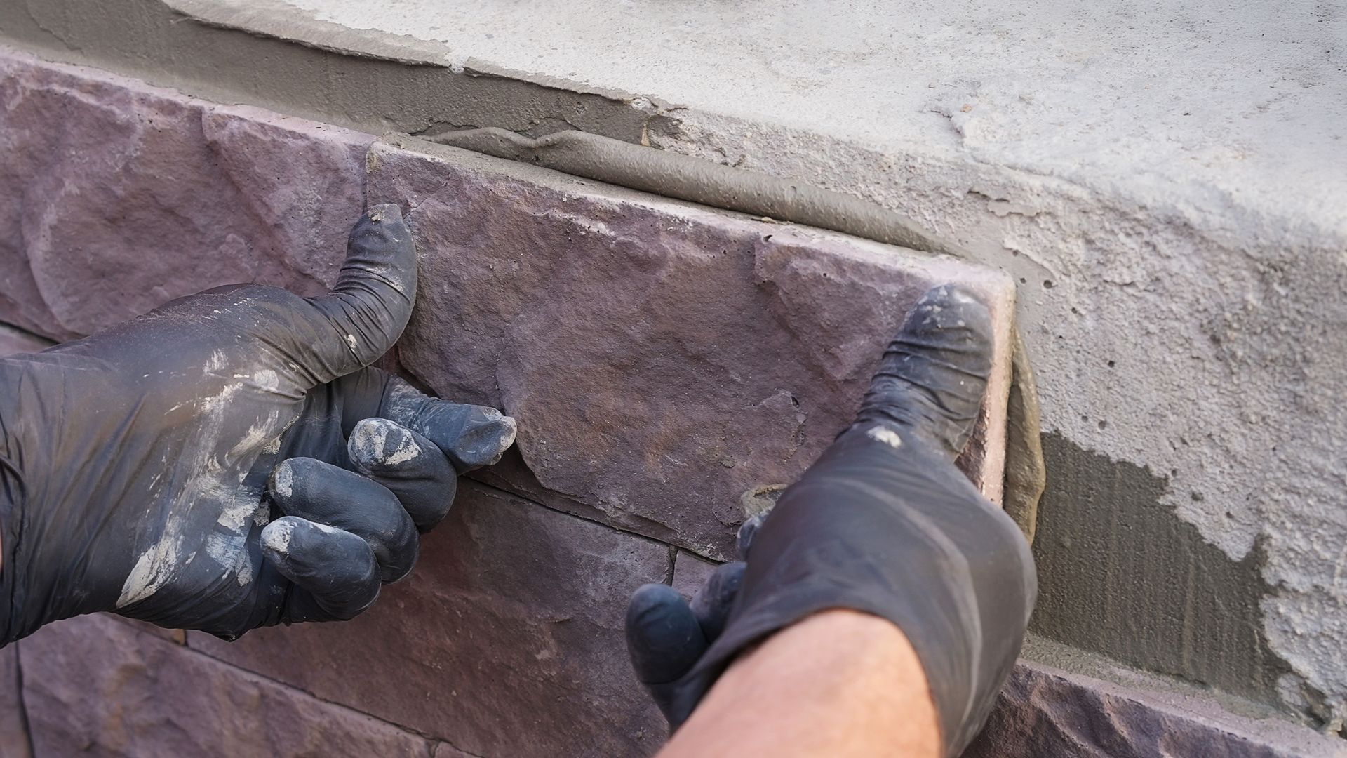 Construction worker installs decorative stone on a wall with mortar.