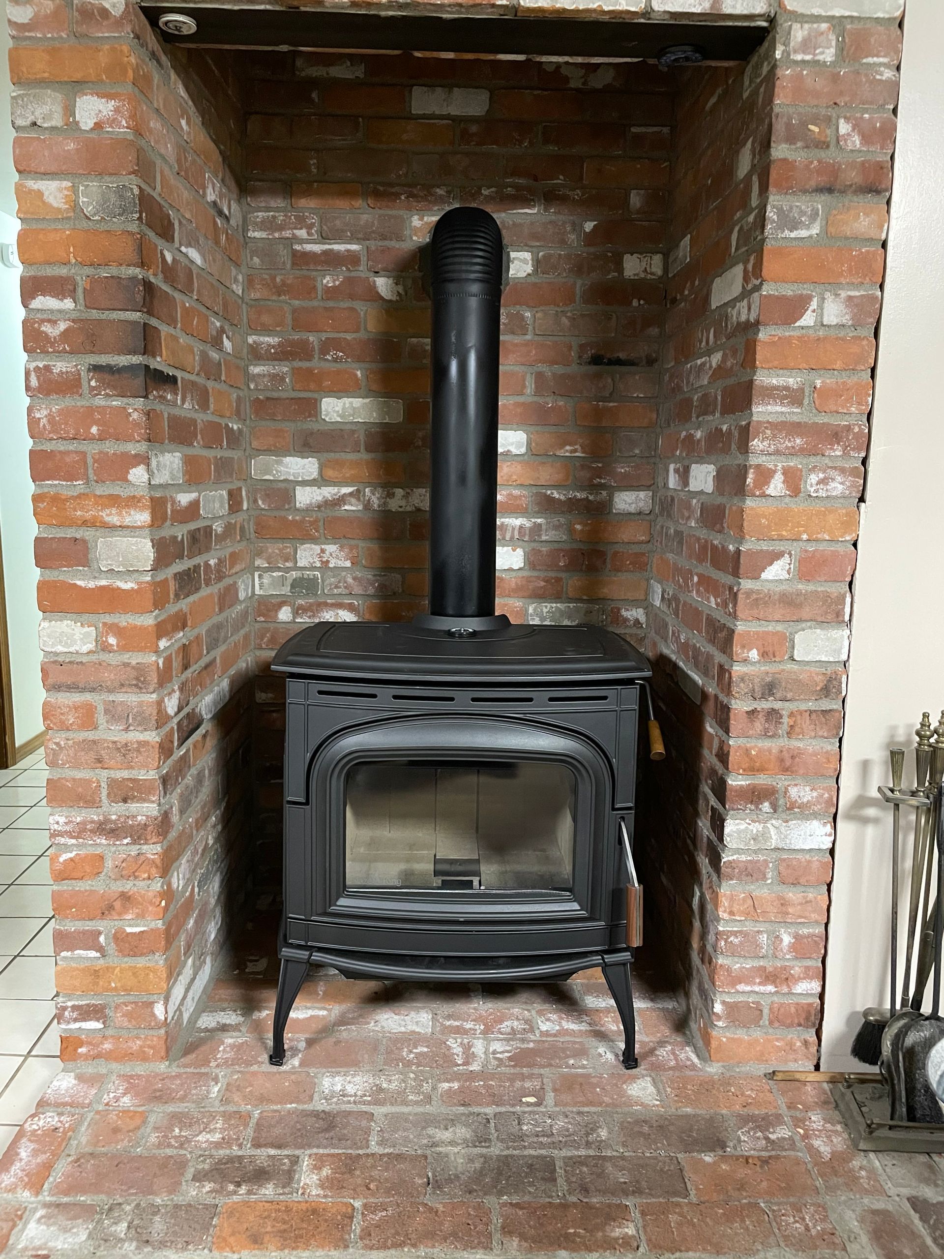 Black wood-burning stove inside a brick fireplace. Chimney pipe extends upwards.