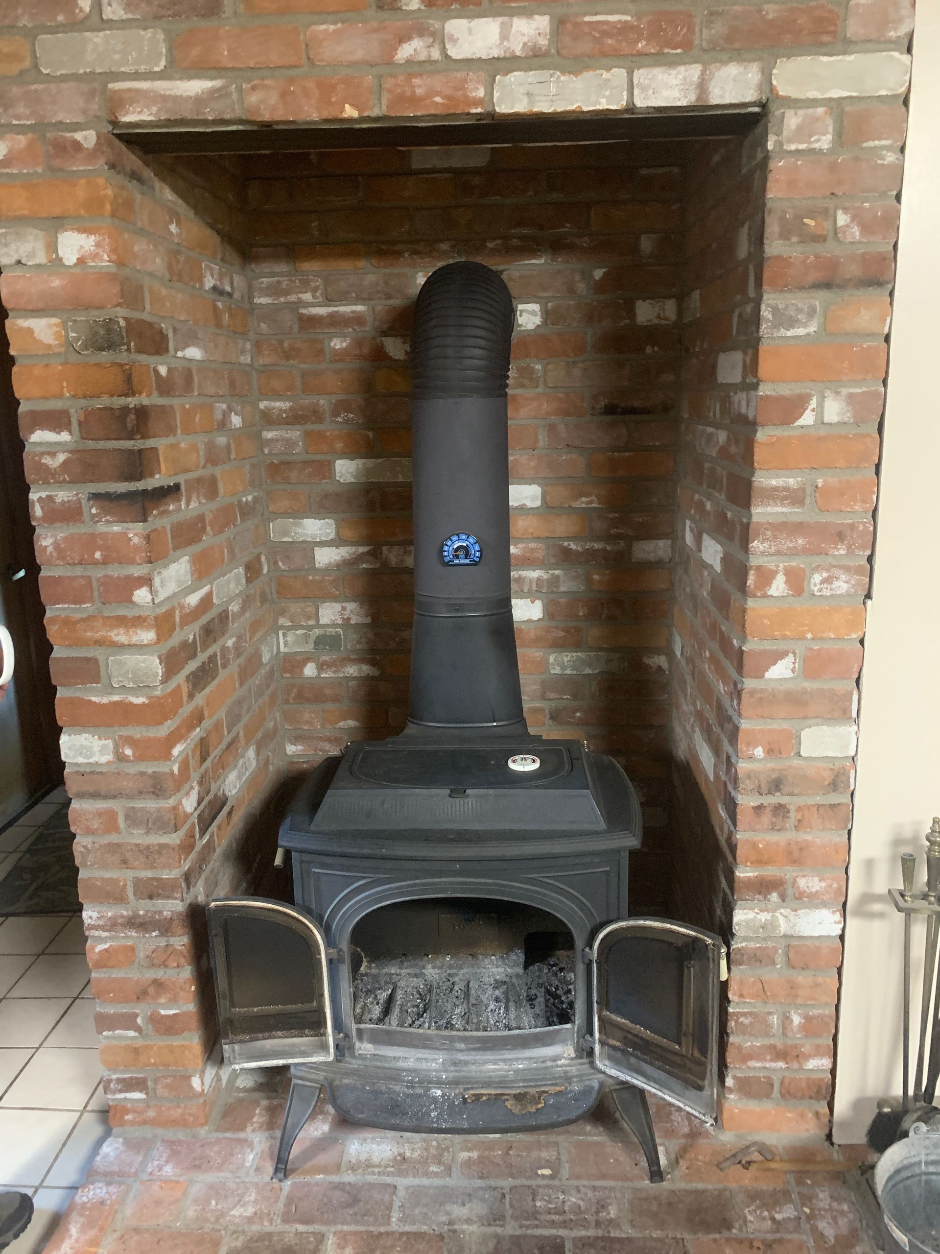 Black wood-burning stove inside a brick fireplace. Doors are open, chimney is black.