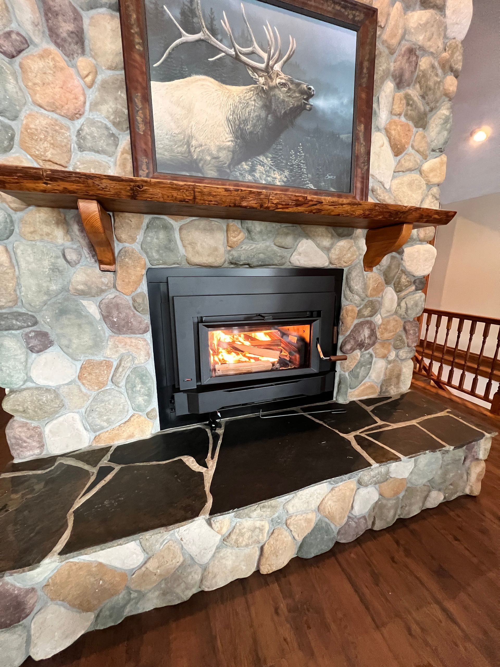Stone fireplace with a burning fire, a wooden mantel, and an elk painting.