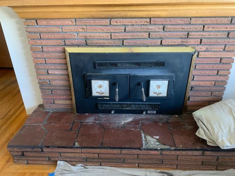 Fireplace with red brick surround and black metal doors. Tiles with flower design.
