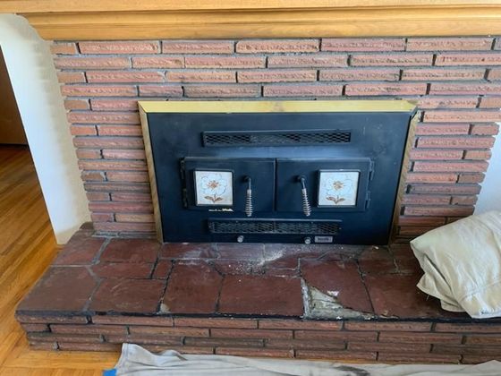 A brick fireplace in a living room with a wooden mantle.