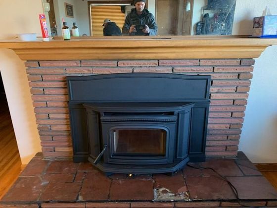 A brick fireplace in a living room with a wooden mantle.