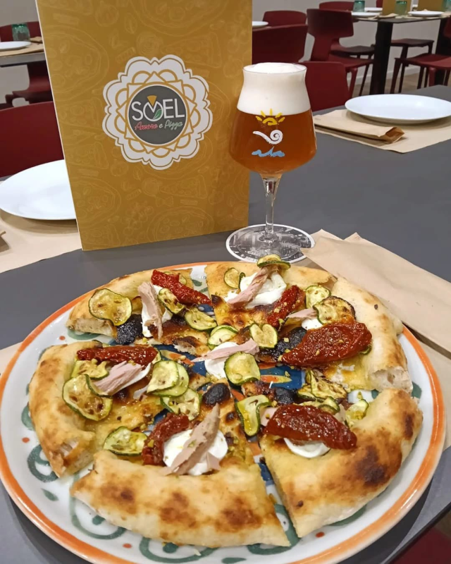 Una pizza su un piatto accanto a un bicchiere di birra