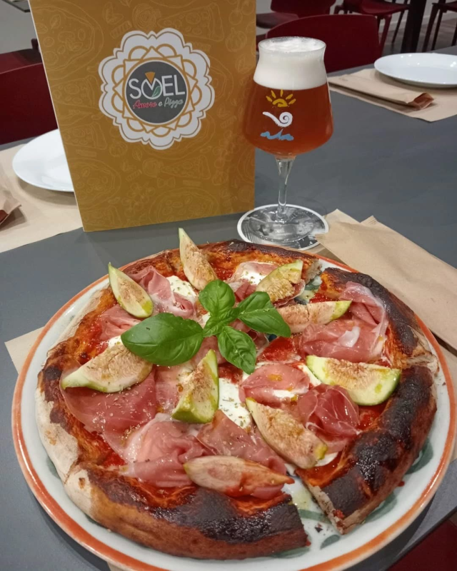 Una pizza è su un piatto accanto a un bicchiere di birra