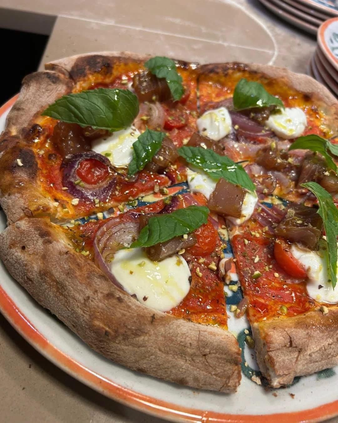 Una pizza con pomodori, cipolle e basilico su un piatto