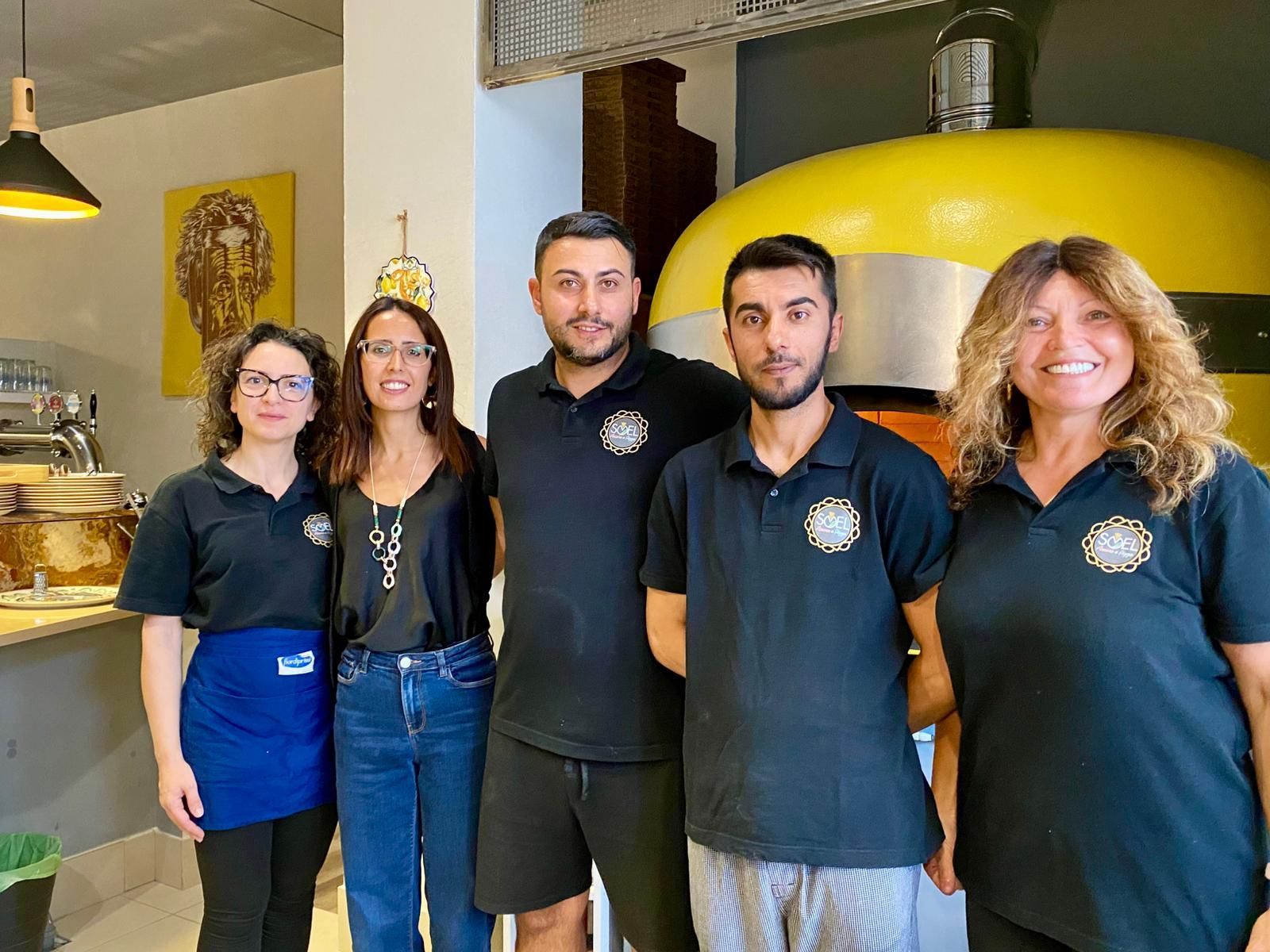 Un gruppo di persone posa per una foto davanti a un forno per pizza.