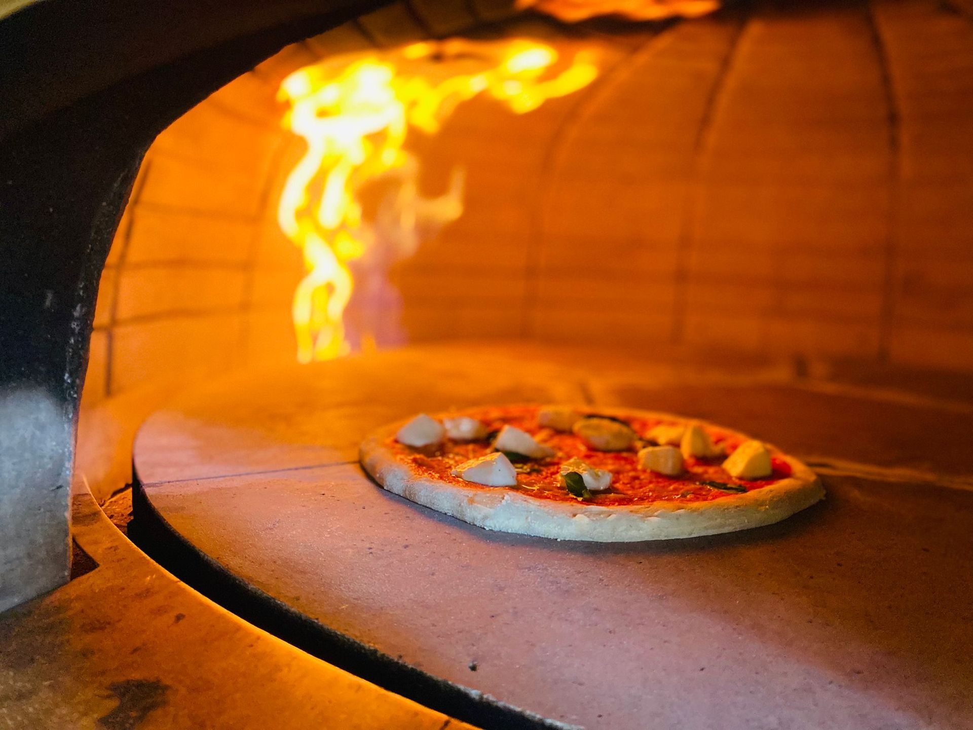 Una pizza viene cotta in un forno da cui escono delle fiamme