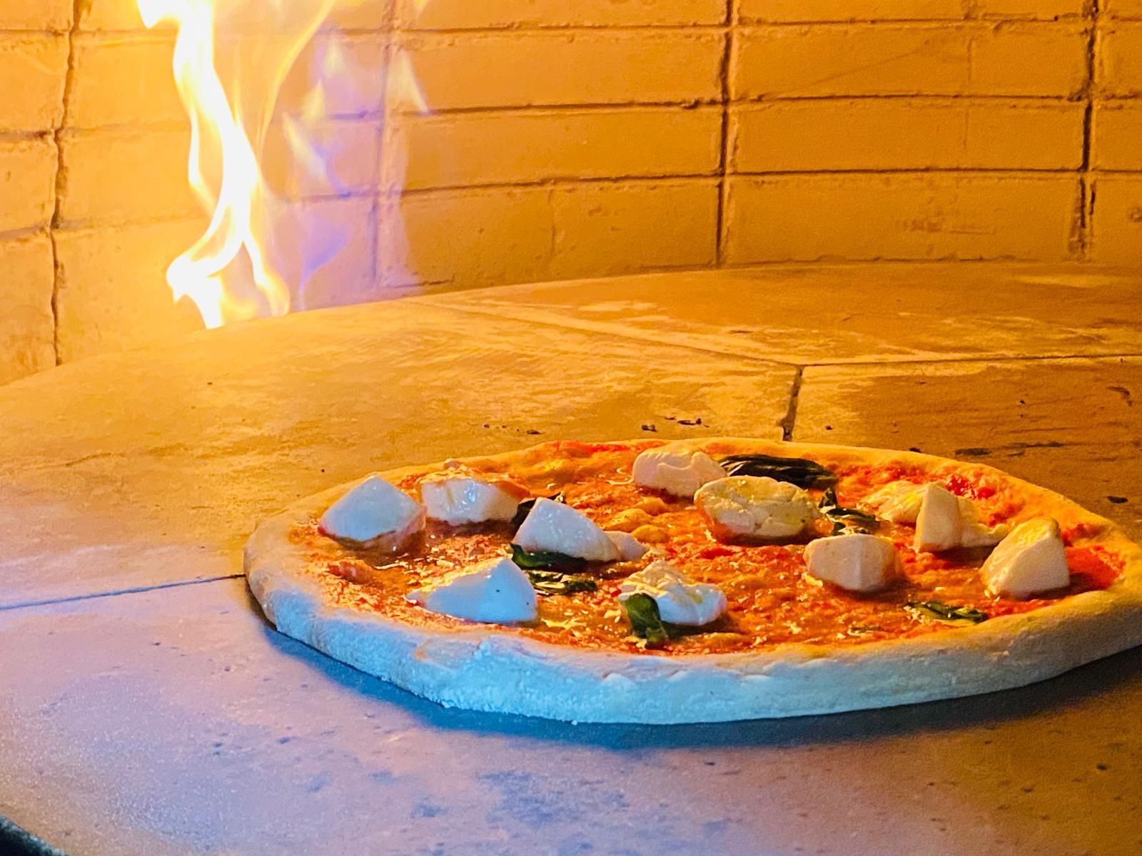 Una pizza viene cotta in un forno con fiamme dietro