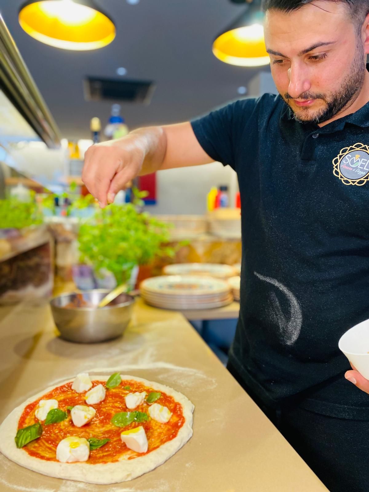 Un uomo con una camicia nera sta preparando una pizza