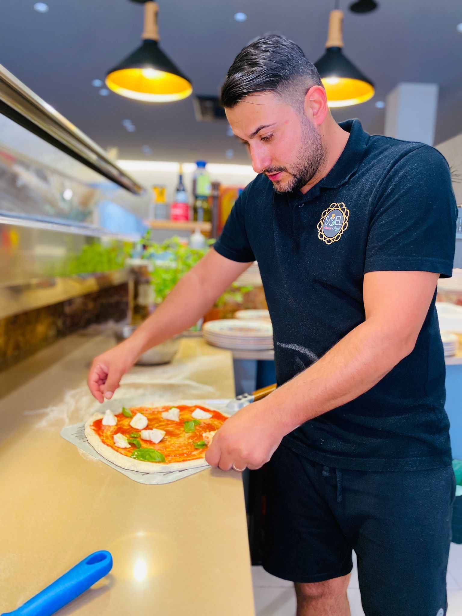 Un uomo con una camicia nera sta preparando una pizza in cucina.
